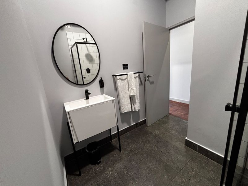 Modern bathroom featuring a sleek vanity with basin, dark tiled flooring, and a glass-enclosed shower with subway tile detailing.