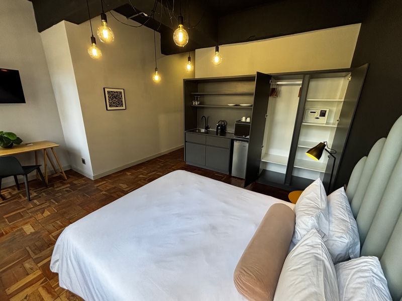 Modern bedroom featuring parquet flooring, an exposed ceiling, and a convenient built-in kitchenette with integrated storage and safe.