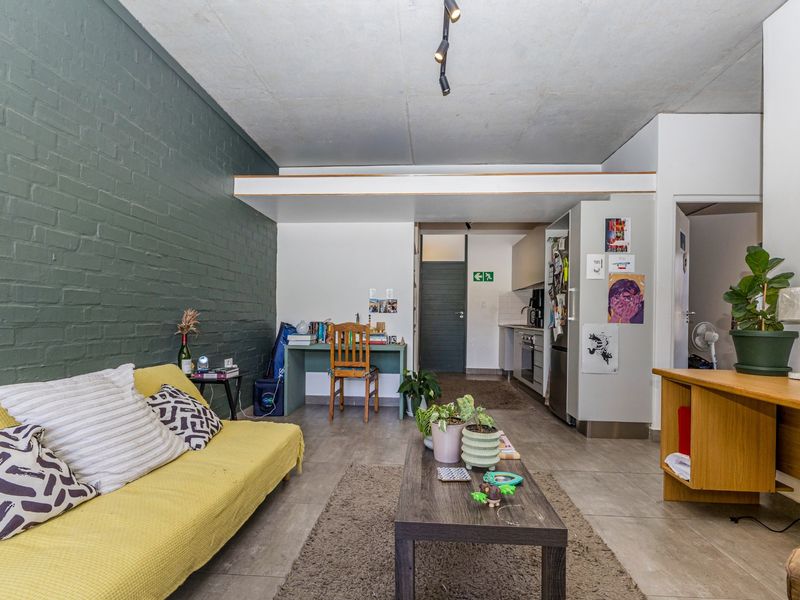 Open-plan living area featuring a painted brick feature wall, tiled flooring, and an integrated kitchen space with built-in cabinetry and appliances.
