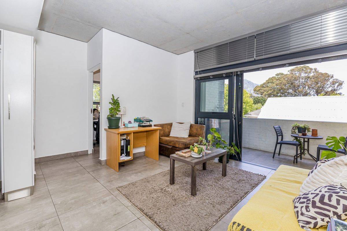 Open-plan living area featuring exposed concrete ceilings, tiled floors, and large sliding doors leading to a private balcony with mountain views.