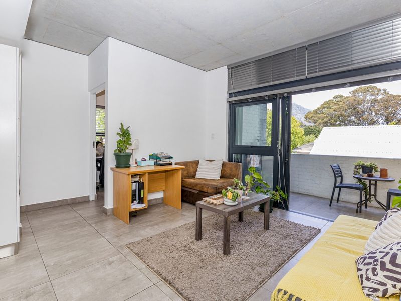 Open-plan living area featuring exposed concrete ceilings, tiled floors, and large sliding doors leading to a private balcony with mountain views.