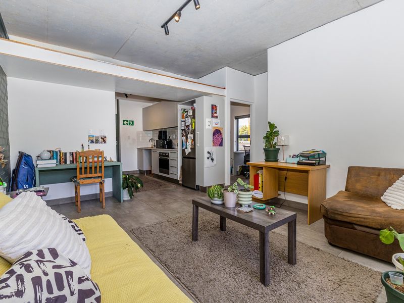 Open-plan living area featuring an exposed concrete ceiling, tiled flooring, and an adjoining kitchen with built-in cabinetry and appliances.
