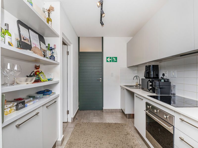 A compact, modern kitchen featuring white cabinetry, built-in oven and hob, tiled backsplash, and integrated shelving for storage.