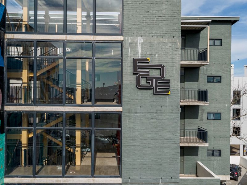 Exterior view of a modern apartment building featuring a painted brick facade, large glass curtain wall, and private balconies.