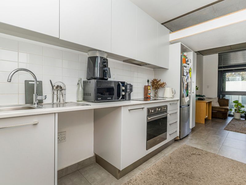 Modern kitchen featuring white cabinetry, tiled backsplash, built-in oven, cooktop, and stainless steel sink, seamlessly flowing into an adjacent living area.