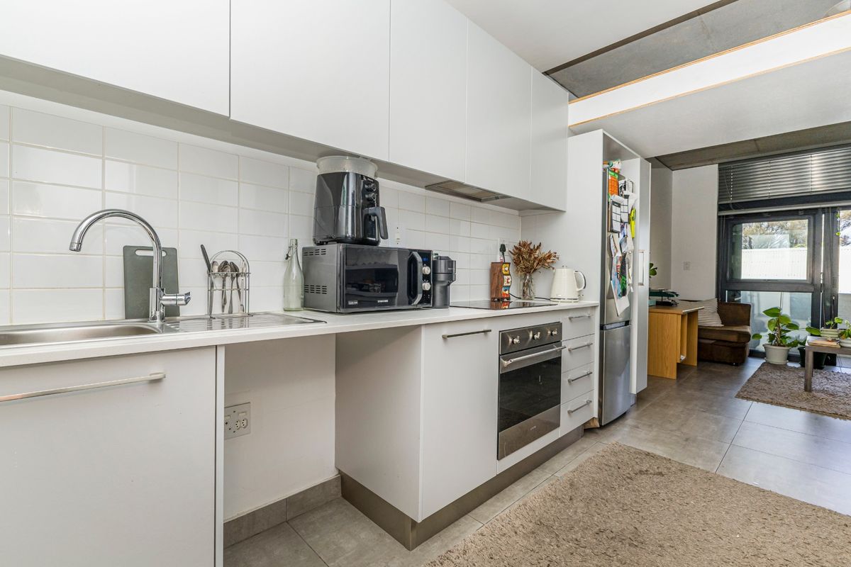 Modern kitchen featuring white cabinetry, tiled backsplash, built-in oven, cooktop, and stainless steel sink, seamlessly flowing into an adjacent living area.