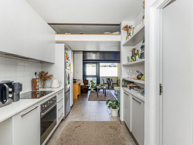 Modern open-plan kitchen and living area featuring sleek white cabinetry, integrated appliances, tiled flooring, and direct access to a private balcony.