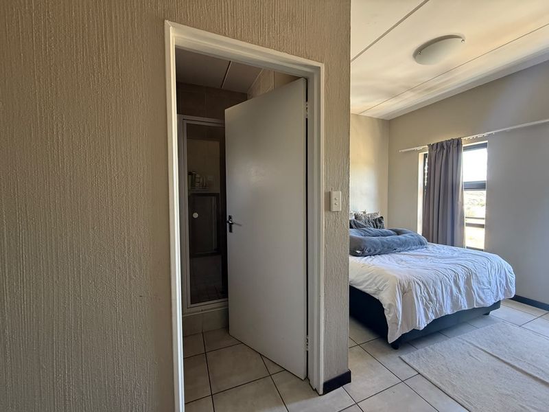 A bedroom featuring tiled flooring and an attached en-suite bathroom with a shower enclosure.
