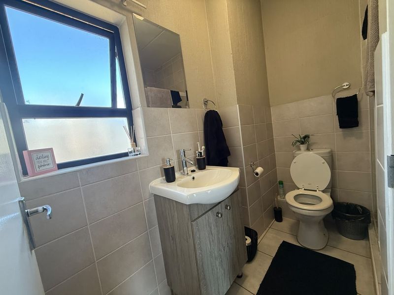 A functional bathroom featuring a vanity cabinet with a ceramic basin, tiled walls, and a top-hung window for natural light.