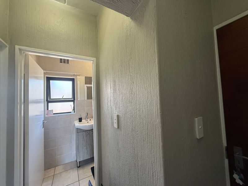 A neutral hallway featuring textured wall finishes and tiled flooring, providing access to an adjacent bathroom with modern vanity and window.