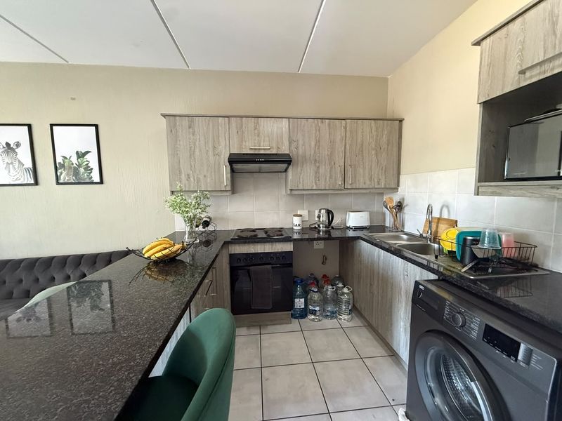 A functional kitchen featuring granite countertops, built-in cabinetry, an electric hob with extractor, and a double sink with tiled flooring and backsplash.