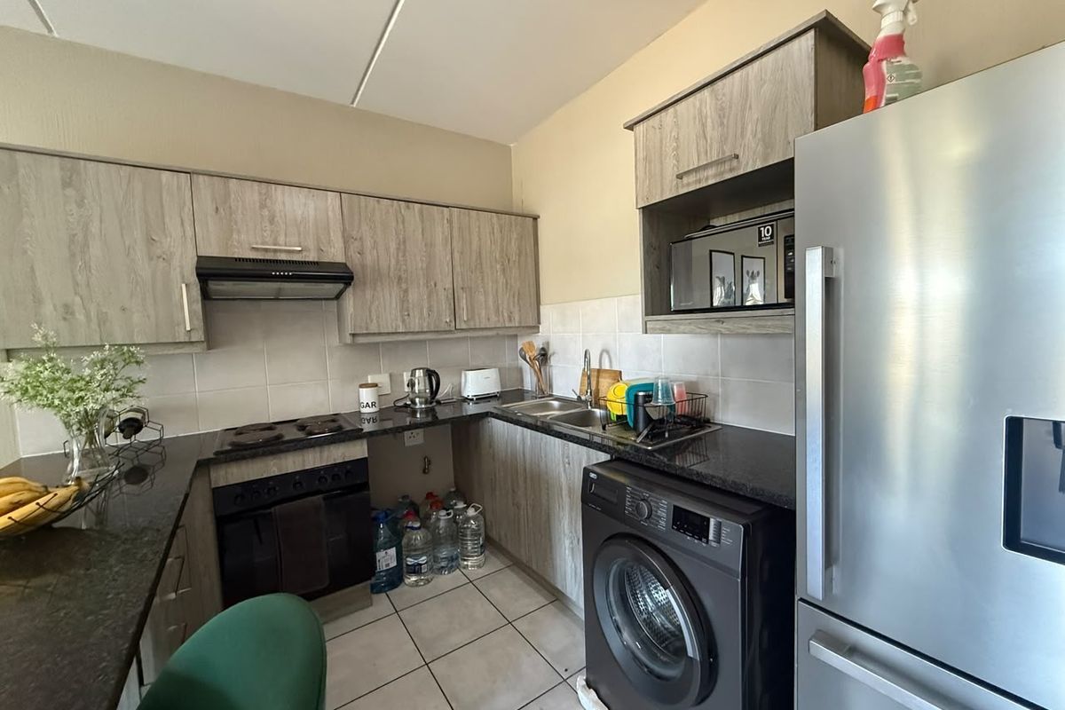 A functional kitchen featuring wood-look laminate cabinetry, granite countertops, a built-in oven with hob, and tiled finishes throughout.