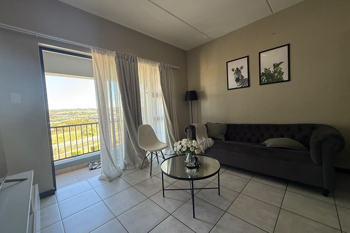 A living room featuring tiled flooring and a sliding glass door that opens onto a balcony with scenic views.