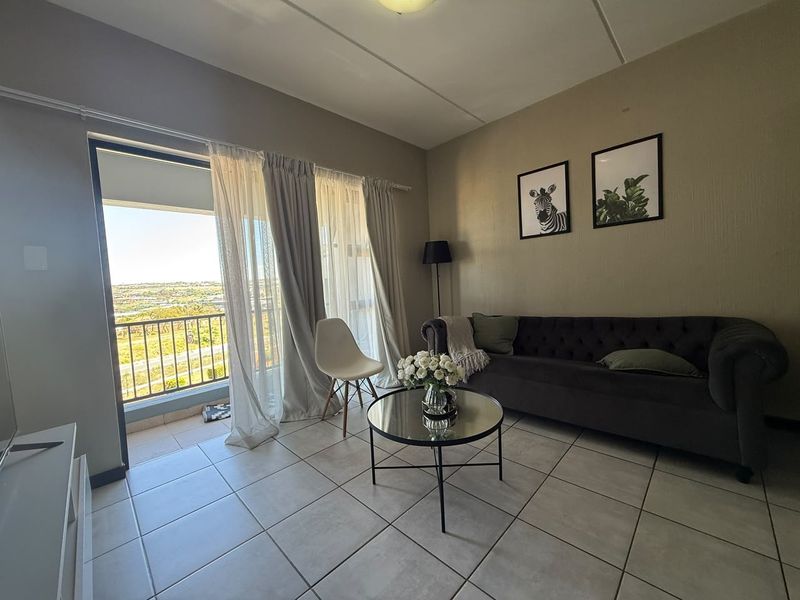 A living room featuring tiled flooring and a sliding glass door that opens onto a balcony with scenic views.