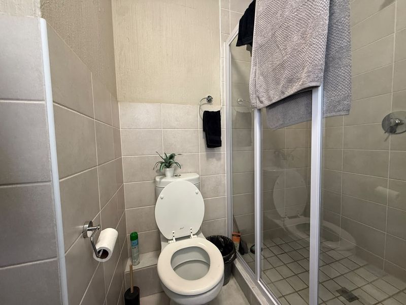 Compact bathroom featuring a toilet and a glass-enclosed shower with neutral wall and floor tiling.