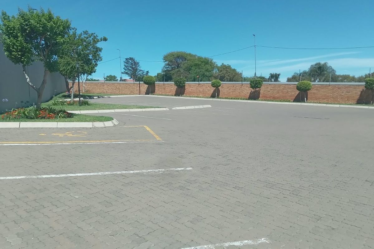 A well-maintained paved parking area featuring a brick boundary wall and landscaped garden beds, providing ample space for residents.