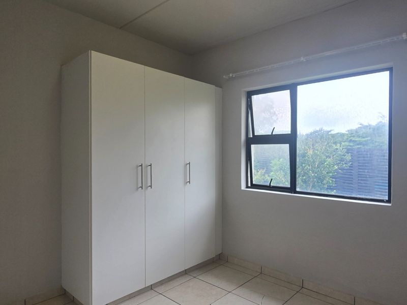 A clean, empty bedroom featuring neutral tiled flooring, a modern built-in wardrobe, and a large window providing natural light.