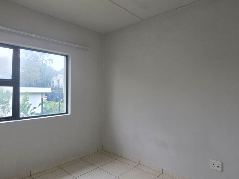 A clean, empty bedroom featuring neutral tiled flooring, a modern aluminium window frame, and a simple curtain rail, ready for personalization.