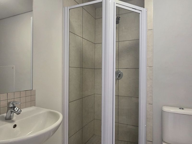 A functional bathroom featuring a shower enclosure, wall-mounted basin, and toilet with neutral tiled finishes.