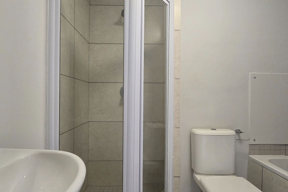 A functional bathroom featuring a shower enclosure, bathtub, toilet, and a wall-mounted washbasin with neutral tiling.