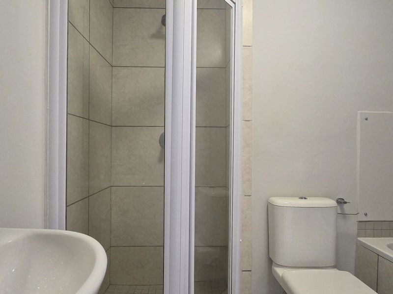 A functional bathroom featuring a shower enclosure, bathtub, toilet, and a wall-mounted washbasin with neutral tiling.