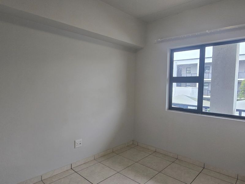 A bright, empty bedroom featuring neutral tiled flooring, built-in cupboards, and a large window providing natural light.