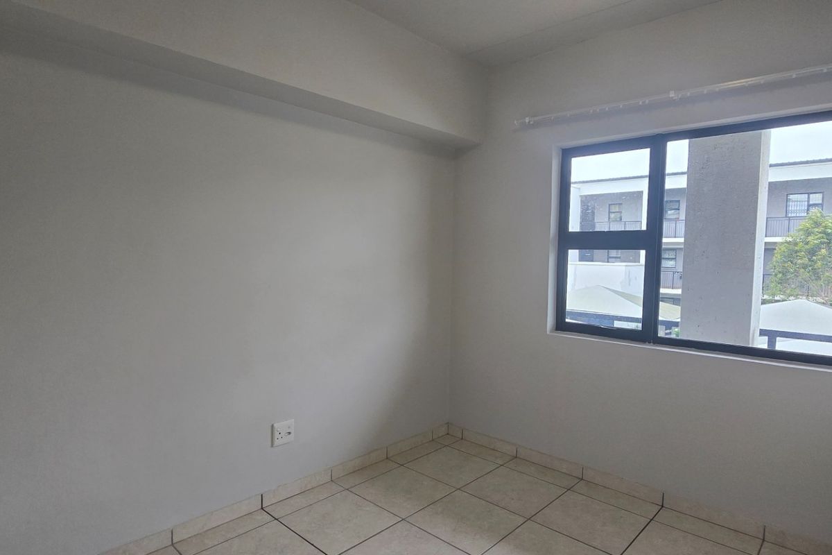 A bright, empty bedroom featuring neutral tiled flooring, built-in cupboards, and a large window providing natural light.