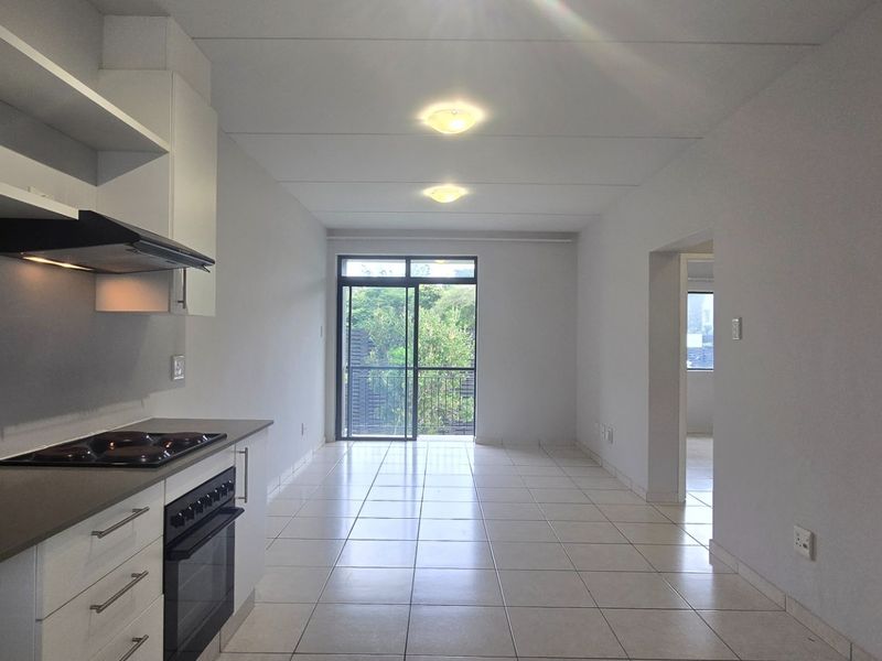A bright, open-plan kitchen and living area featuring tiled floors, modern cabinetry, built-in appliances, and direct access to a balcony through sliding glass doors.