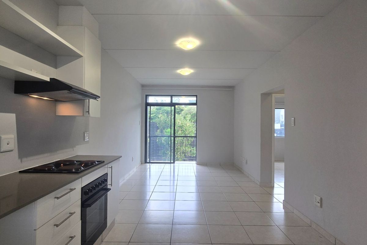 A bright, open-plan kitchen and living area featuring tiled floors, modern cabinetry, built-in appliances, and direct access to a balcony through sliding glass doors.