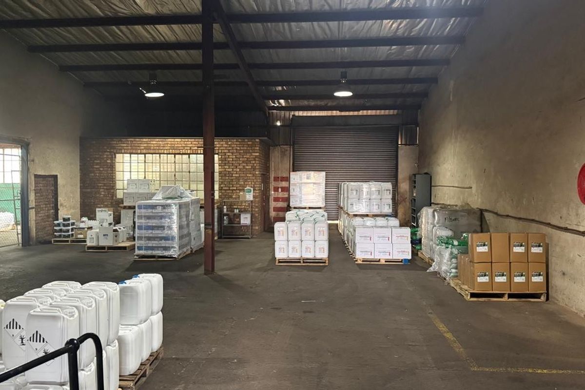 Spacious industrial warehouse unit featuring high ceilings with exposed steel trusses, a large roller shutter door, and durable concrete flooring.
