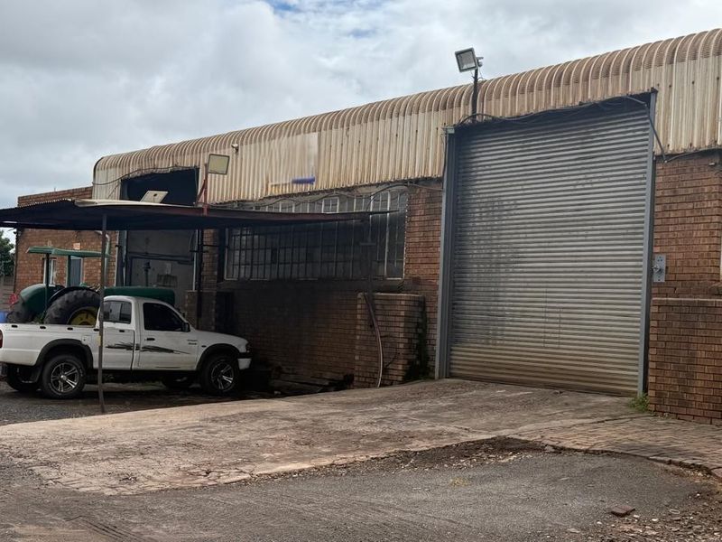 Industrial warehouse exterior featuring a large roller shutter door, brick facade, and corrugated metal roofing with an adjacent concrete driveway.