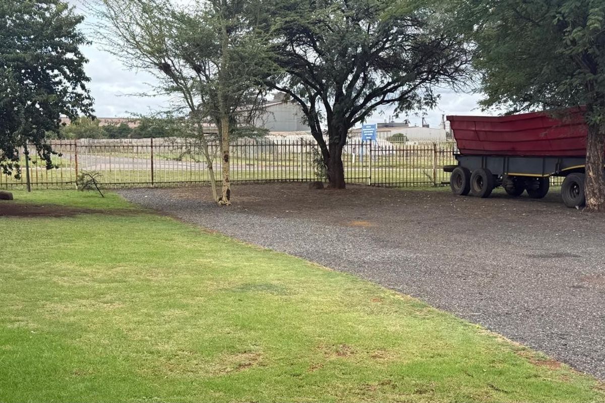 A view of the industrial property's rear yard featuring a gravel driveway, lawn area, and metal perimeter fencing.