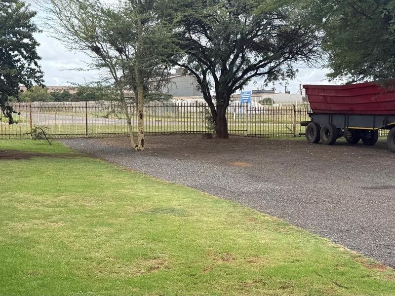 A view of the industrial property's rear yard featuring a gravel driveway, lawn area, and metal perimeter fencing.