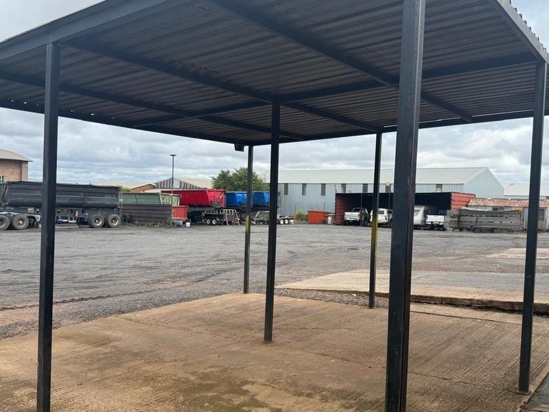 Open-sided industrial steel-framed shelter with a corrugated metal roof and concrete slab flooring, suitable for vehicle or equipment storage.