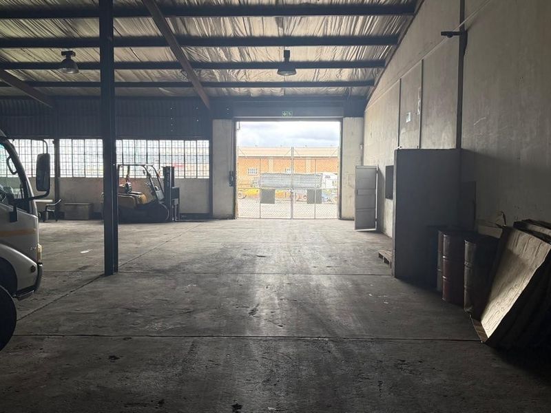 Spacious industrial warehouse unit featuring high ceilings, concrete flooring, and a large roller shutter door for vehicle access.