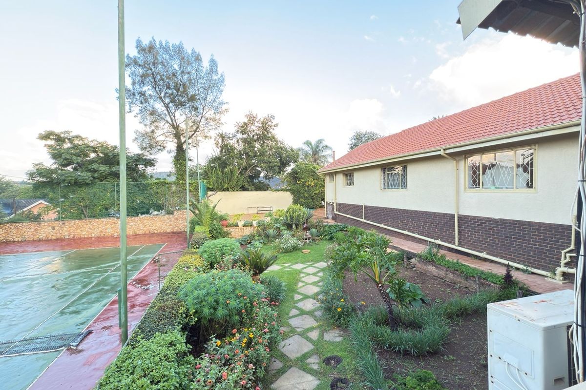 Rear exterior view featuring a private tennis court, landscaped garden with stone pathways, and the side elevation of the house with a tiled roof.