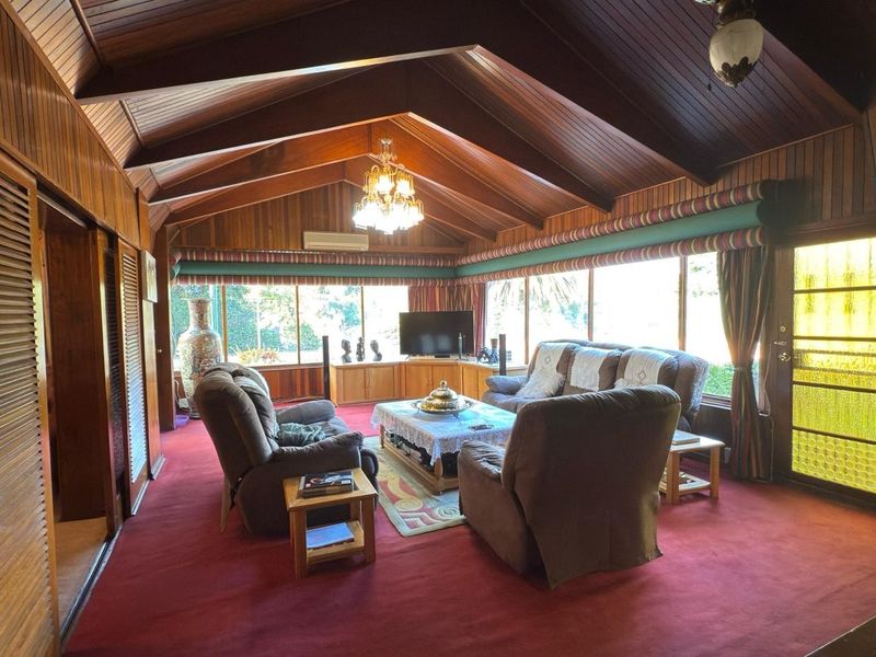 Spacious living room featuring a high vaulted timber ceiling, extensive wood wall paneling, built-in cabinetry, and large windows providing ample natural light.