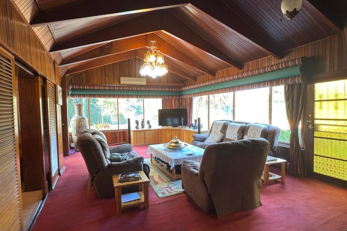 Spacious living room featuring a high vaulted timber ceiling, extensive wood wall paneling, built-in cabinetry, and large windows providing ample natural light.