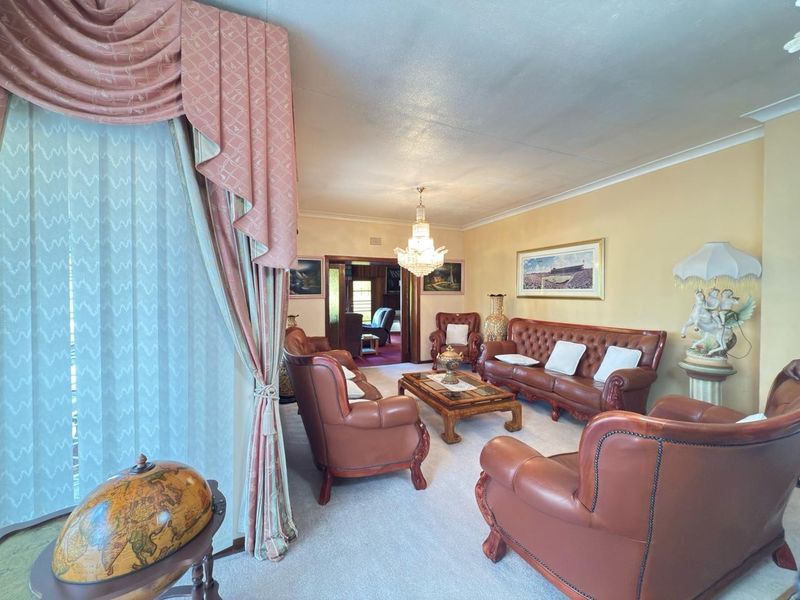 A spacious living room featuring a crystal chandelier, coved ceiling cornices, and large sliding glass doors leading to the exterior.