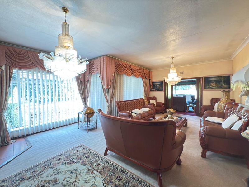 Spacious living room featuring elegant crystal chandeliers, large sliding glass doors, and neutral carpeting, offering a classic and well-lit formal lounge area.