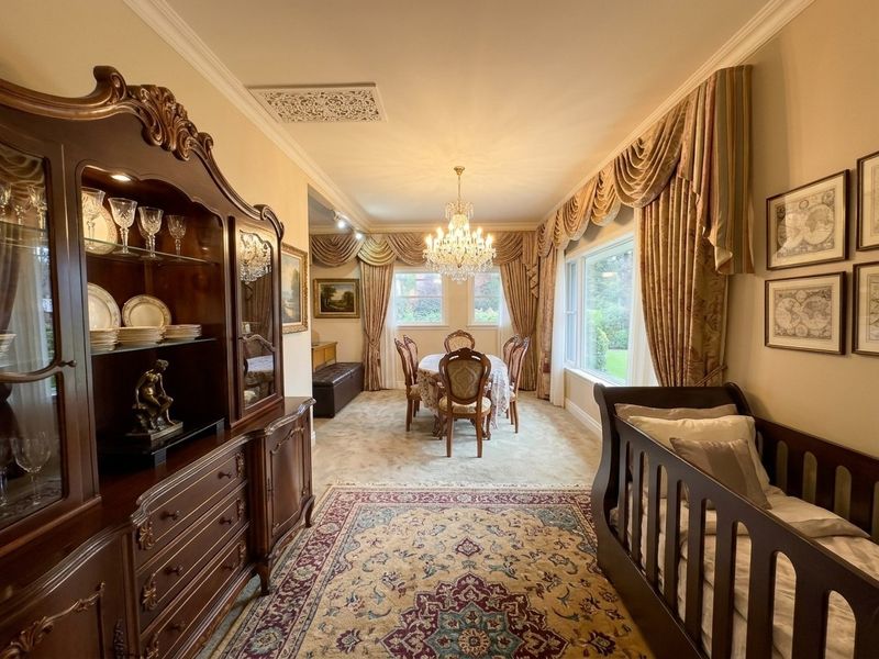 A formal dining room featuring a crystal chandelier, decorative cornicing, and large windows overlooking the garden, providing a classic and elegant atmosphere.