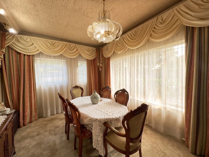 A formal dining room featuring a decorative chandelier, fitted window pelmets, and security bars, offering a traditional layout ready for modern updates.