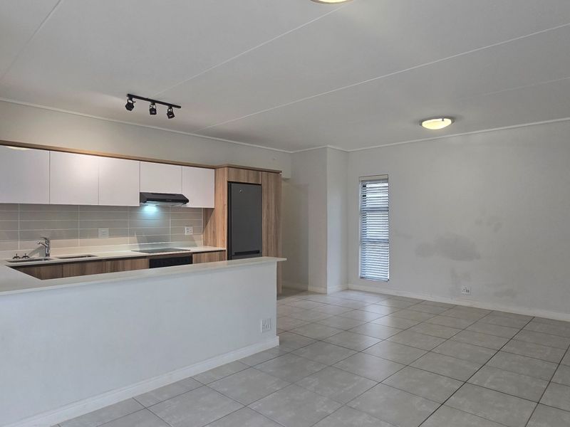 An open-plan kitchen and living area featuring modern cabinetry, a breakfast bar, tiled flooring, and neutral finishes, ready for personalization.