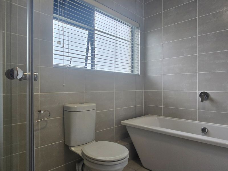 Modern bathroom featuring a freestanding bathtub, separate shower enclosure, and neutral grey wall tiling with natural light from a window.