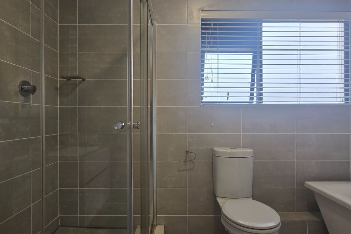 Modern bathroom featuring a glass shower enclosure, a bathtub, and neutral wall tiling, complemented by a window with fitted blinds.