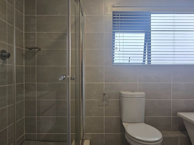 Modern bathroom featuring a glass shower enclosure, a bathtub, and neutral wall tiling, complemented by a window with fitted blinds.