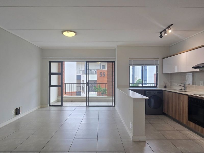 Modern open-plan living area featuring tiled floors, a sleek kitchen with built-in appliances, and direct access to a private balcony.