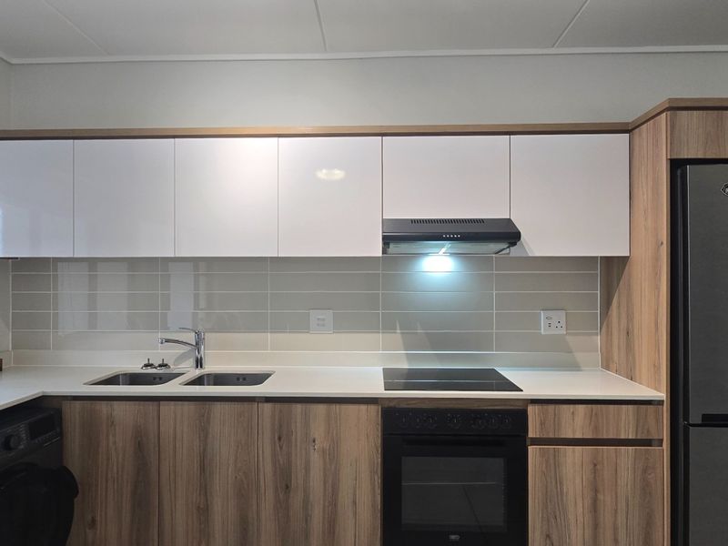 Modern kitchen featuring sleek white and wood-grain cabinetry, stone countertops, integrated appliances, and a tiled backsplash.