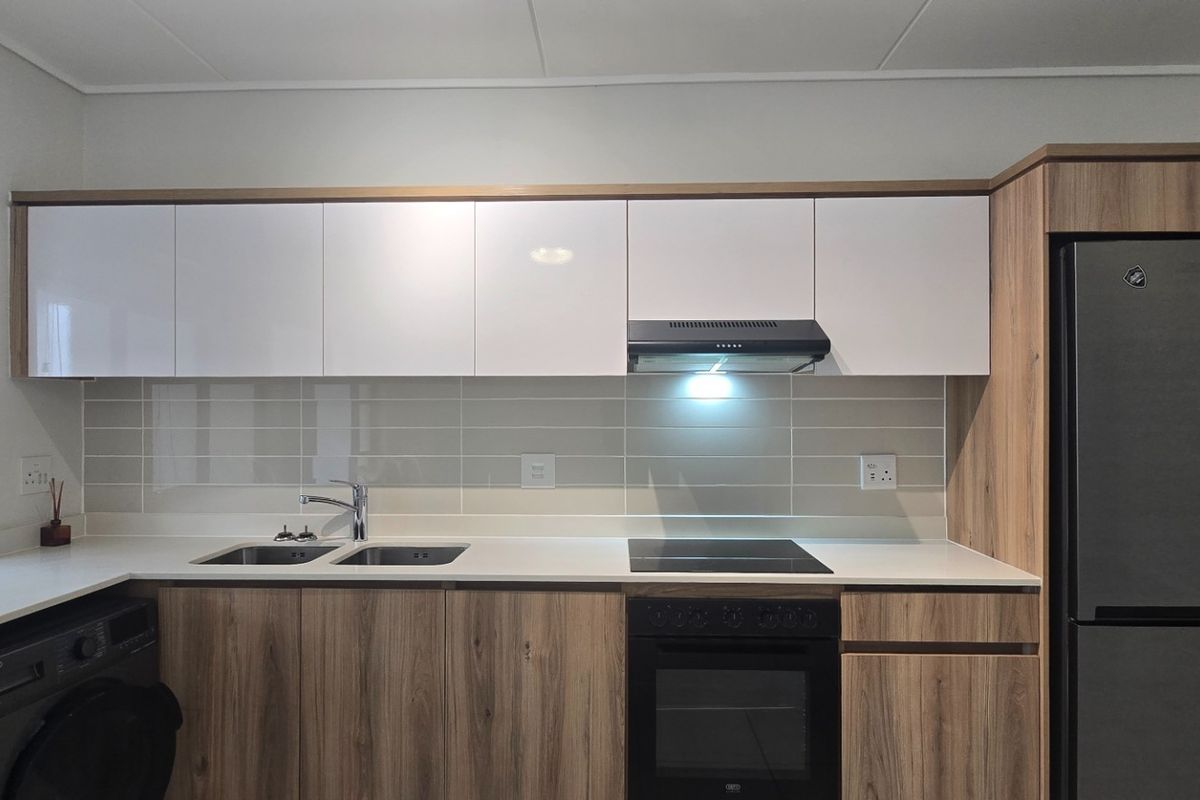 Modern kitchen featuring sleek white and wood-grain cabinetry, stone countertops, integrated appliances, and a tiled backsplash.