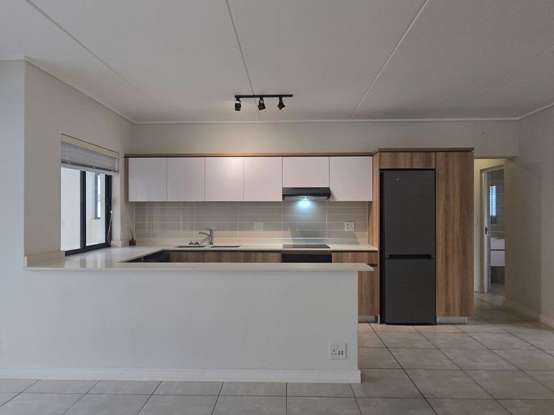 Modern open-plan kitchen featuring sleek cabinetry, stone countertops, and integrated appliances, seamlessly flowing into the living area with access to a private balcony.